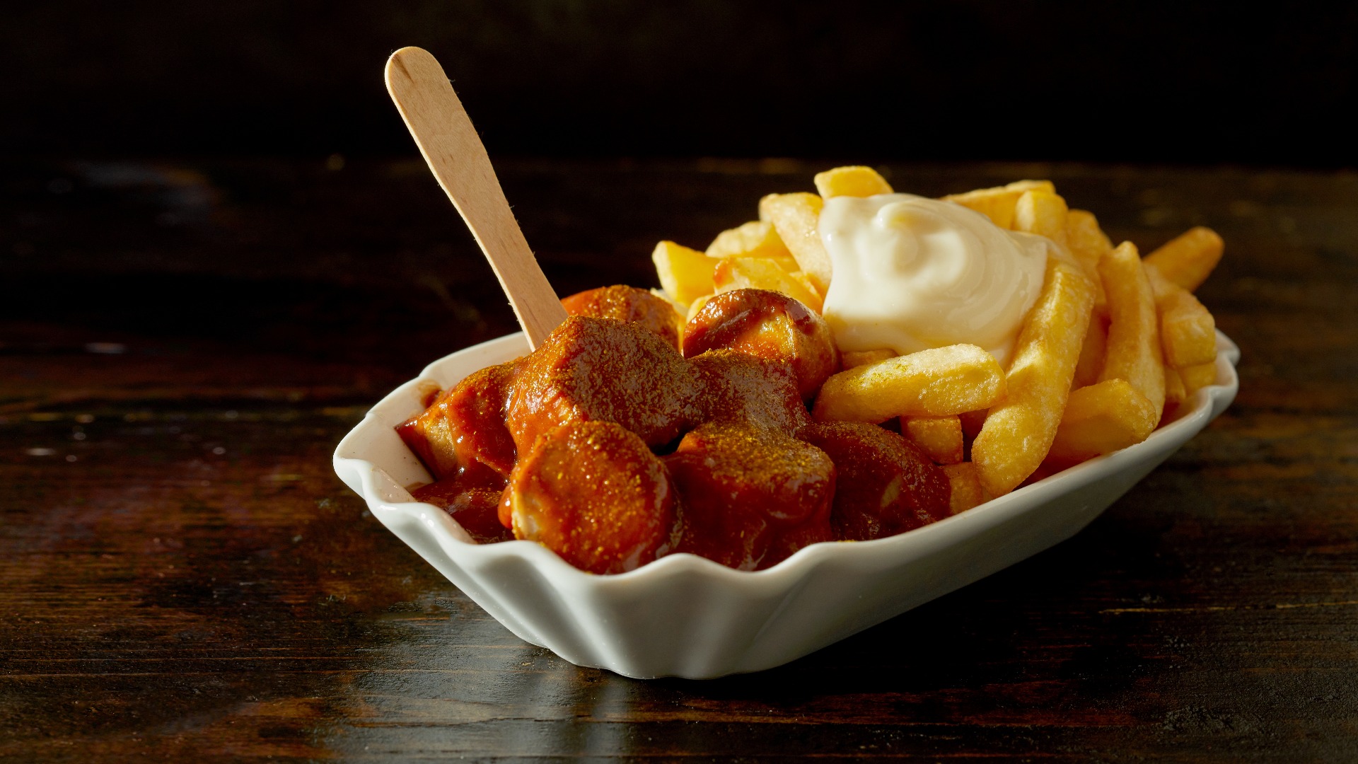 Currywurst mit scharfen Pommes frites und Saucen in Schale