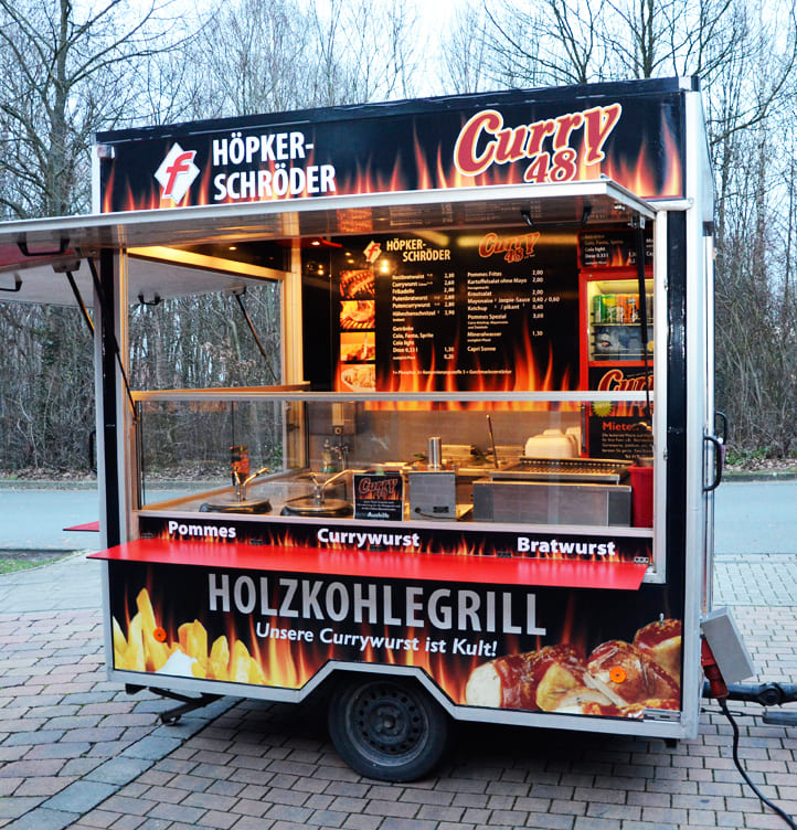 Imbisswagen mit schwarzer und roter Feueroptik bietet Currywurst und Pommes an