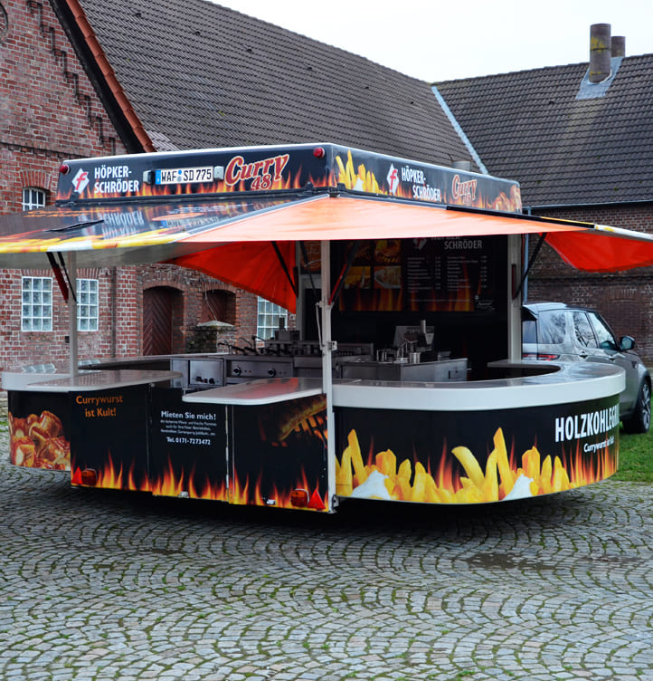 Ein farbenfroher Imbisswagen mit Pommes und Currywurst Motiven steht auf Pflastersteinen