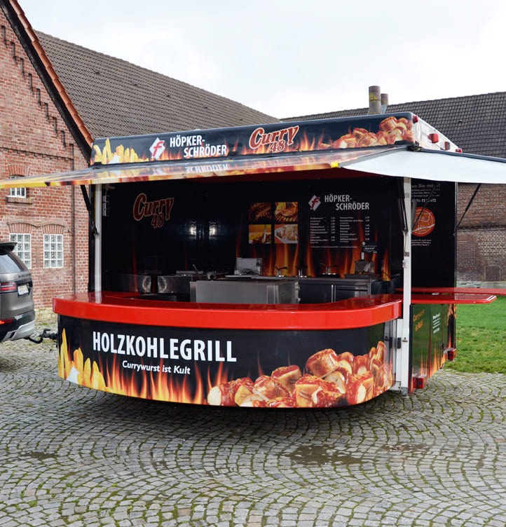 Ein leerer schwarz-roter Imbisswagen mit Holzkohlegrill auf einem gepflasterten Platz