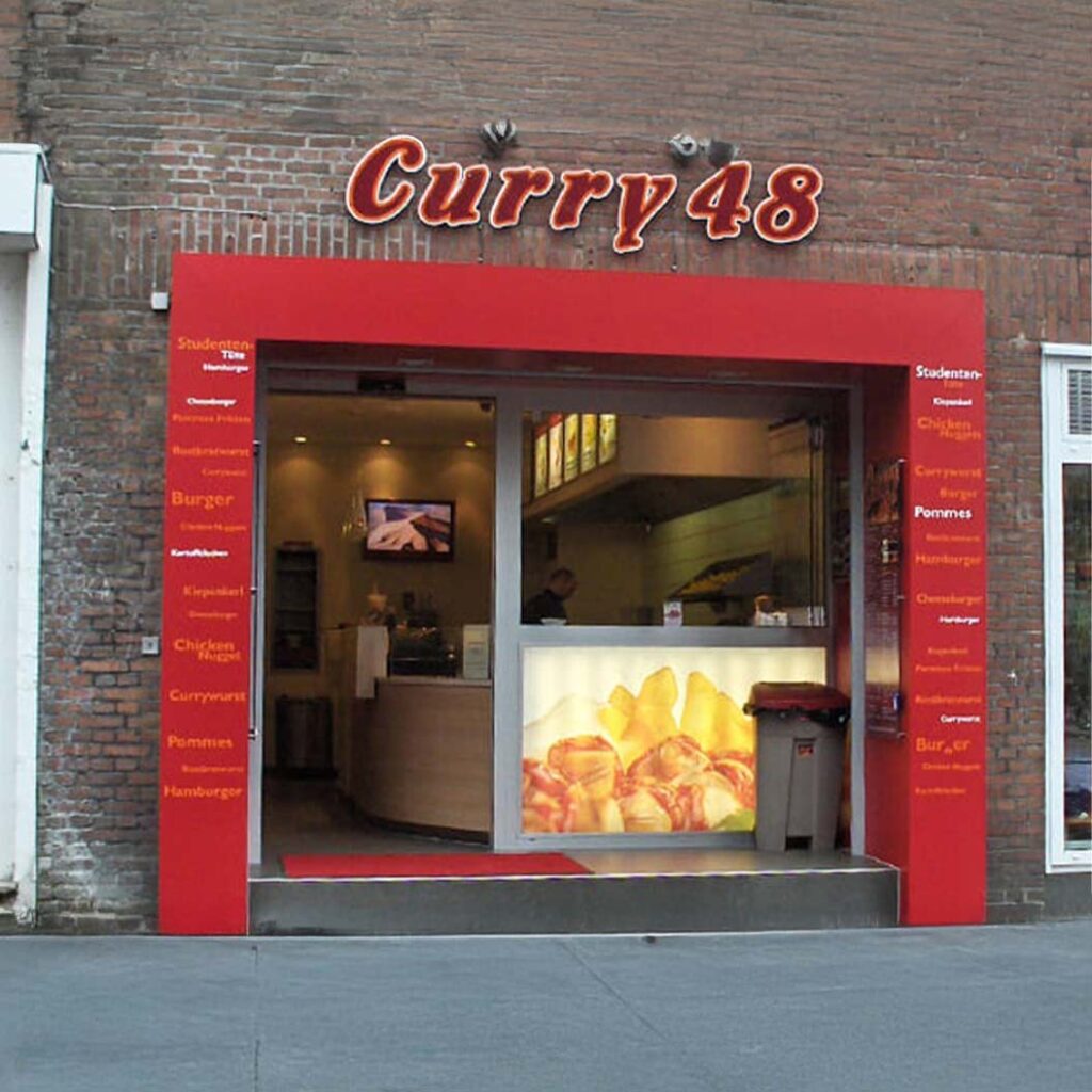 Ein Imbiss namens Curry 48 mit rotem Rahmen und großem Foto von Currywurst