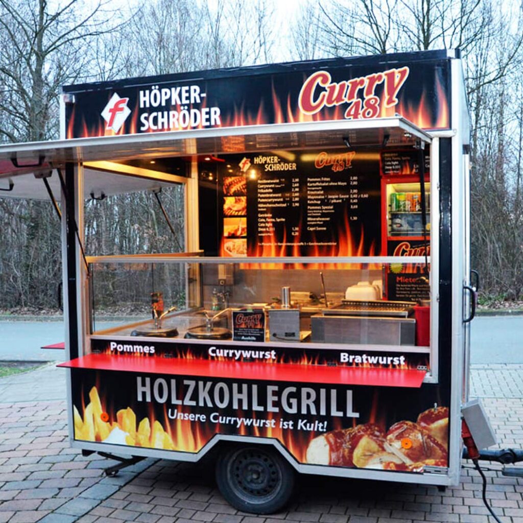 Ein mobiler Imbisswagen mit Holzkohlegrill, leuchtender Flammenoptik und Speisekarte
